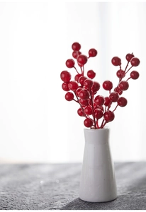 Close-up of vibrant red artificial berries in a white ceramic vase for Christmas decor