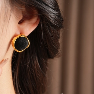 Gros plan d'une boucle d'oreille carrée dorée avec détail de flocage noir sur modèle