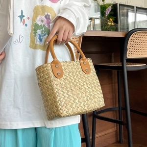 Detail of hand-woven straw handbag featuring premium brown leather handles and metal rivets