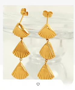 Detailed view of polished golden triple-layered fan-shaped drop earrings hanging on a glass
