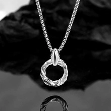 Macro detail of silver box chain and textured metal ring pendant on dark rock