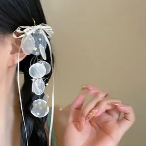 Detail of a white bow hairclip with long ribbons and translucent shell-like round charms