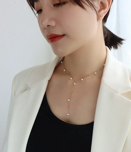 Detail of 18k gold-plated pearl Y-necklace with tassels on a model wearing a white blazer
