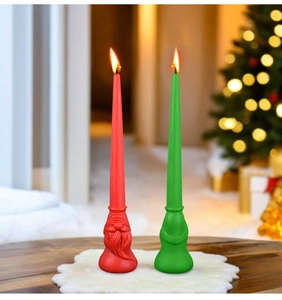 Detail showing two lit Christmas gnome-shaped candles on a white fuzzy mat and wood surface