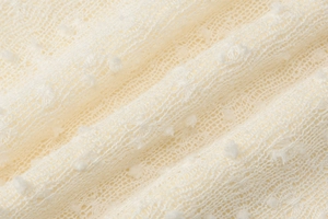 Detailed macro view of cream knitted fabric featuring delicate 3D textured polka dots