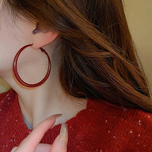 Close-up of model wearing large burgundy red glossy hoop earrings for a stylish look
