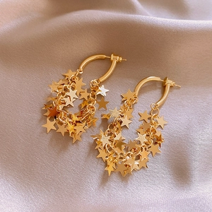 Detail view of gold layered star pendant earrings on beige silk fabric background