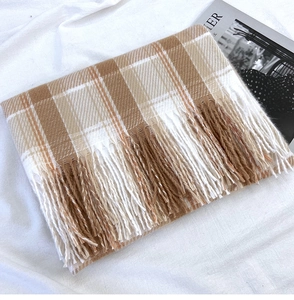 Detail shot of brown plaid scarf with fringe edges and orange accents on linen fabric