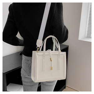 Detail of white leather crossbody bag with wide fabric strap and metal pendant shown on model