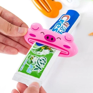 Pink pig-shaped manual toothpaste squeezer being used on a tube with a white background