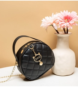 Detail of black quilted mini bag with gold chain and cat charm next to pink flowers