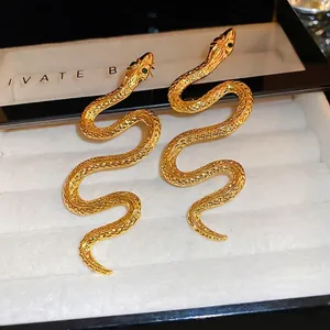 Golden snake drop earrings with green crystal eyes on white velvet jewelry box