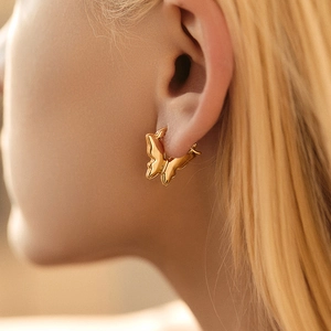 Close-up of golden butterfly hoop earrings with polished finish on a model's ear