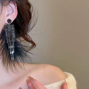 Gros plan sur de longues boucles d'oreilles à pompons noirs avec strass et plumes
