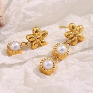 Detail of asymmetric gold floral earrings with hanging pearls on a textured white surface