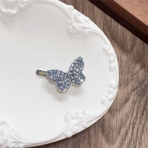 Detailed macro shot of a blue rhinestone butterfly hair clip on a vintage white tray