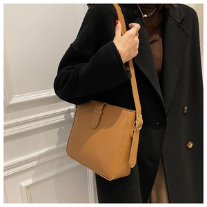 Detailed view of brown leather bucket shoulder bag worn with a stylish black coat