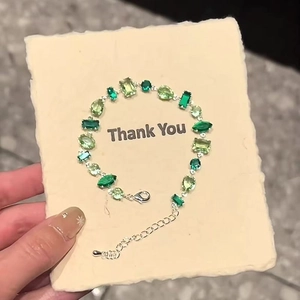 Close-up of a silver bracelet with gradient green gemstones on a thank you card