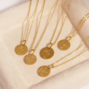 Detailed view of six gold titanium steel necklaces with oval floral pendants on a beige tray