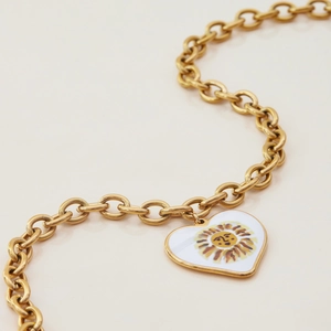 Close-up of golden chain necklace with white heart pendant and vintage sun face design