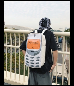 Outdoor view of a white retro mobile phone backpack with orange screen and keypad prints