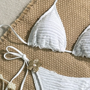 Detail of white bikini with textured fabric and a gold flower pearl accessory