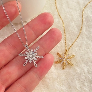 Dettaglio di collane a fiocco di neve in oro e argento con zirconi su sfondo di peluche