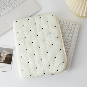 Close-up of quilted cream laptop sleeve with black dots and smooth metal zipper detail