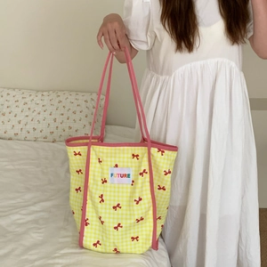 Detail of yellow plaid canvas tote bag with pink straps and red bow print design