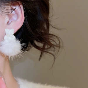 Close-up of white plush bear earrings with pearl necklace detail worn by a model