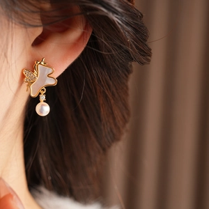 Détail de boucles d'oreilles papillon dorées avec perles, zircones et nacre élégante
