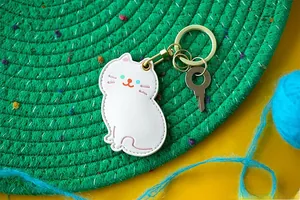 Détail du porte-carte chat blanc en cuir litchi avec anneau de clé doré et coutures