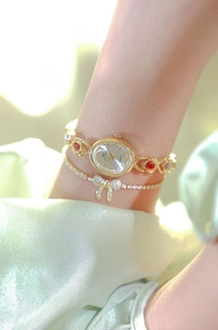 Close-up of gold oval watch with colorful crystals and matching bow bracelet on wrist
