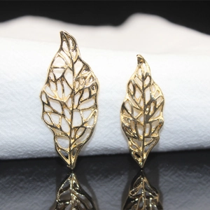 Close-up of golden hollow leaf charms in two sizes on white fabric with mirror reflection