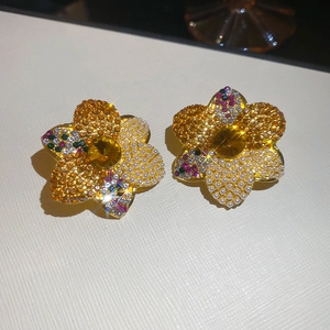 Close-up of golden floral earrings with yellow crystals, pearls, and sparkling details
