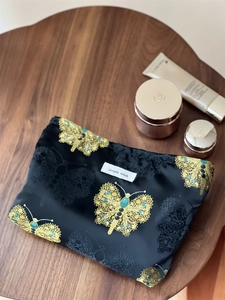 Close-up of black jacquard makeup bag with gold butterfly patterns and brand label