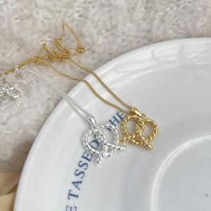 Detailed close-up of gold and silver twisted rope heart necklaces in a white dish