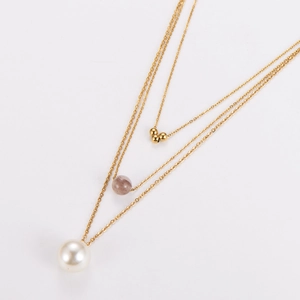 Détail du collier doré multi-rangs avec perle blanche et pendentif perle taupe sur fond blanc