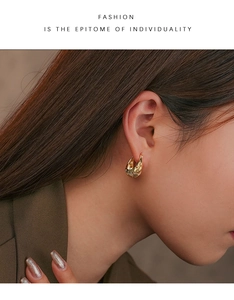 Close-up of golden textured hoop earring with woven pattern worn by a model in a suit