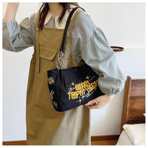 Detail of black canvas tote bag with colorful embroidery and metal chain leather strap