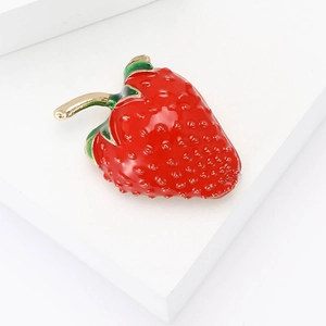 Minimalist red strawberry enamel brooch with green leaves and gold finish on white stand