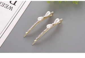 Detail view of two gold pearl bobby pins with teardrop pearls and crystals on green base