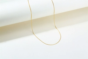Detail shot of a minimalist 1mm golden snake chain necklace on a white roll prop