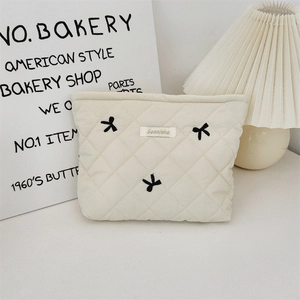 Detailed shot of quilted ivory toiletry bag featuring black bow embroidery and fabric label