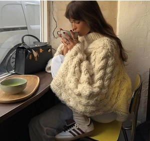 Detailed knit texture of cream oversized crewneck sweater in cozy cafe setting