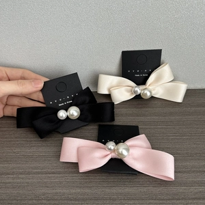 Close-up of three satin bow hair clips with pearls in black, ivory, and pink colors