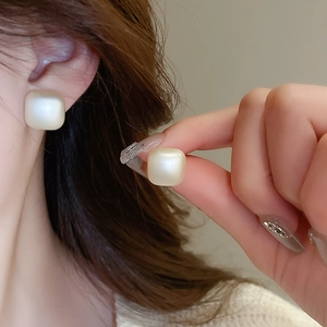 Detailed close-up of matte square pearl earrings worn and held to show texture