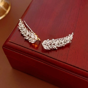 Detail of silver leaf ear cuffs with sparkling zircons and pearls on a wooden box