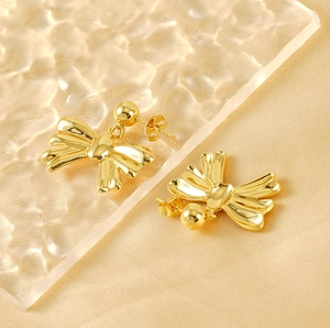 Close-up of elegant 18k gold-plated stainless steel bow earrings on silk fabric
