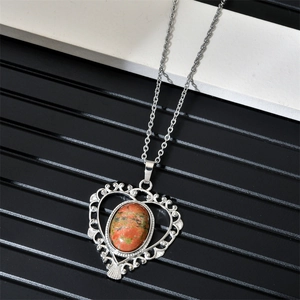 Close-up of heart-shaped silver necklace with natural green and red stone pendant
